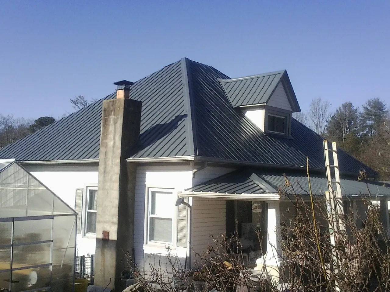 Dark blue standing seam metal roof on a white farmhouse with dormer — Slate & Tile Roof Repair by Roofing Brothers in Riley