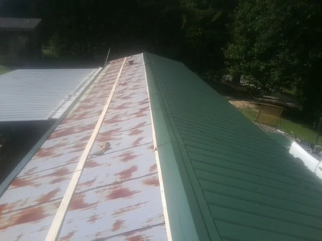 Old rusted panels beside newly installed green metal roofing — Wind Damage Roof Repair by Roofing Brothers in Riley